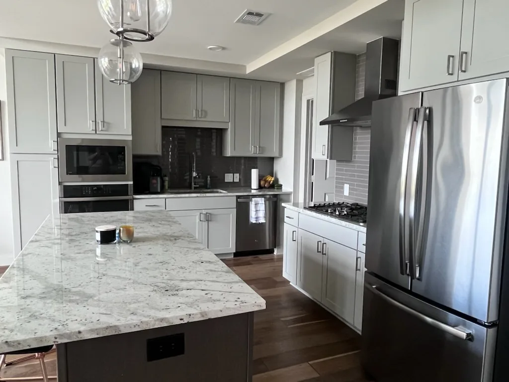 Modern kitchen with white cabinetry, granite countertop island, stainless steel appliances, and black backsplash.