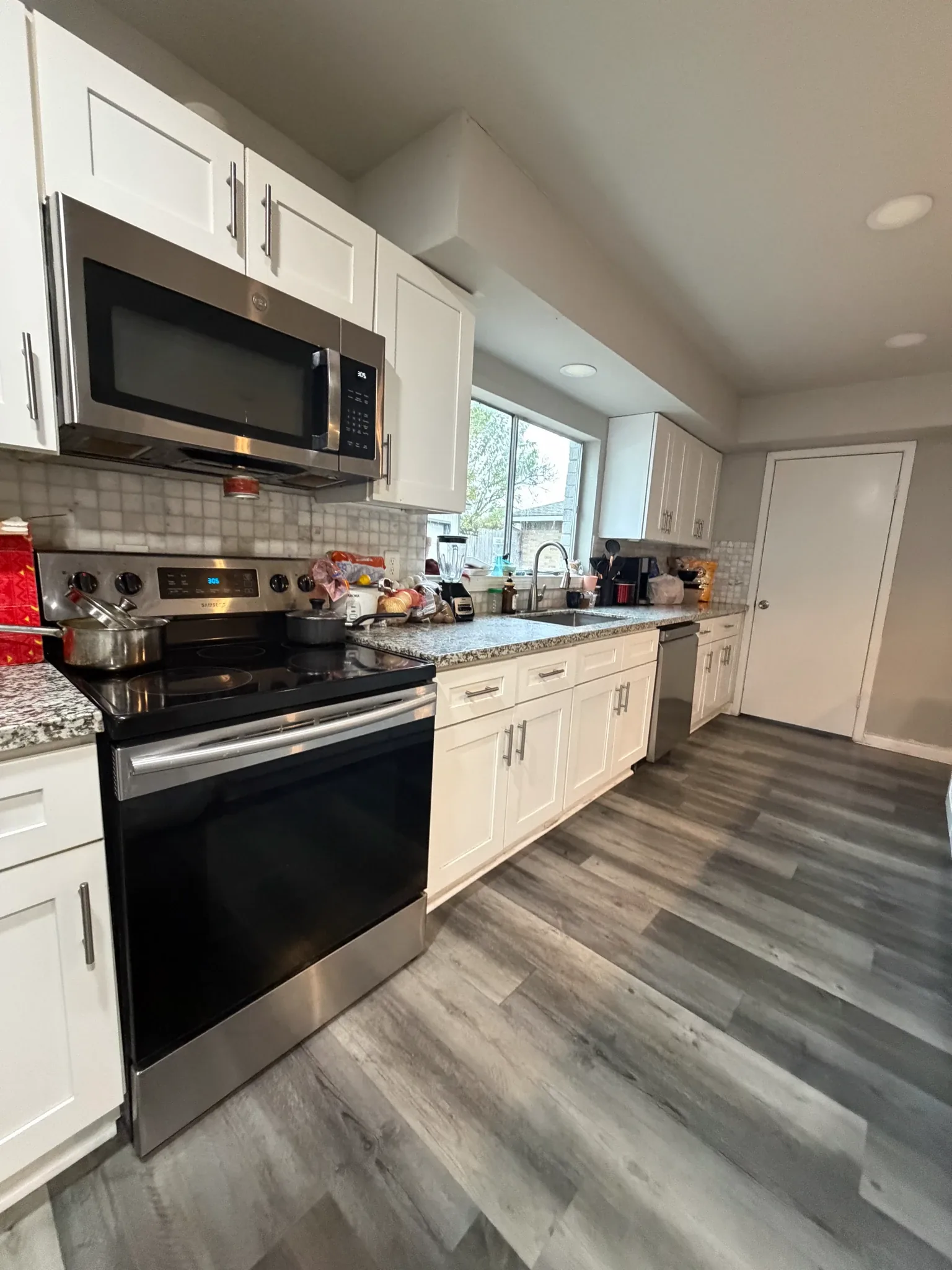 Modern kitchen with white cabinets, stainless steel appliances, granite countertops, and wood-look flooring.